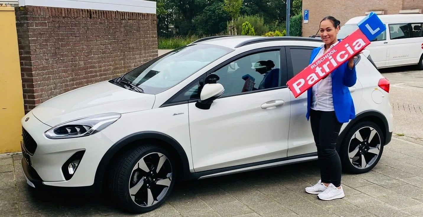 Patricia naast de lesauto, met het lesbord van Rijschool Patricia